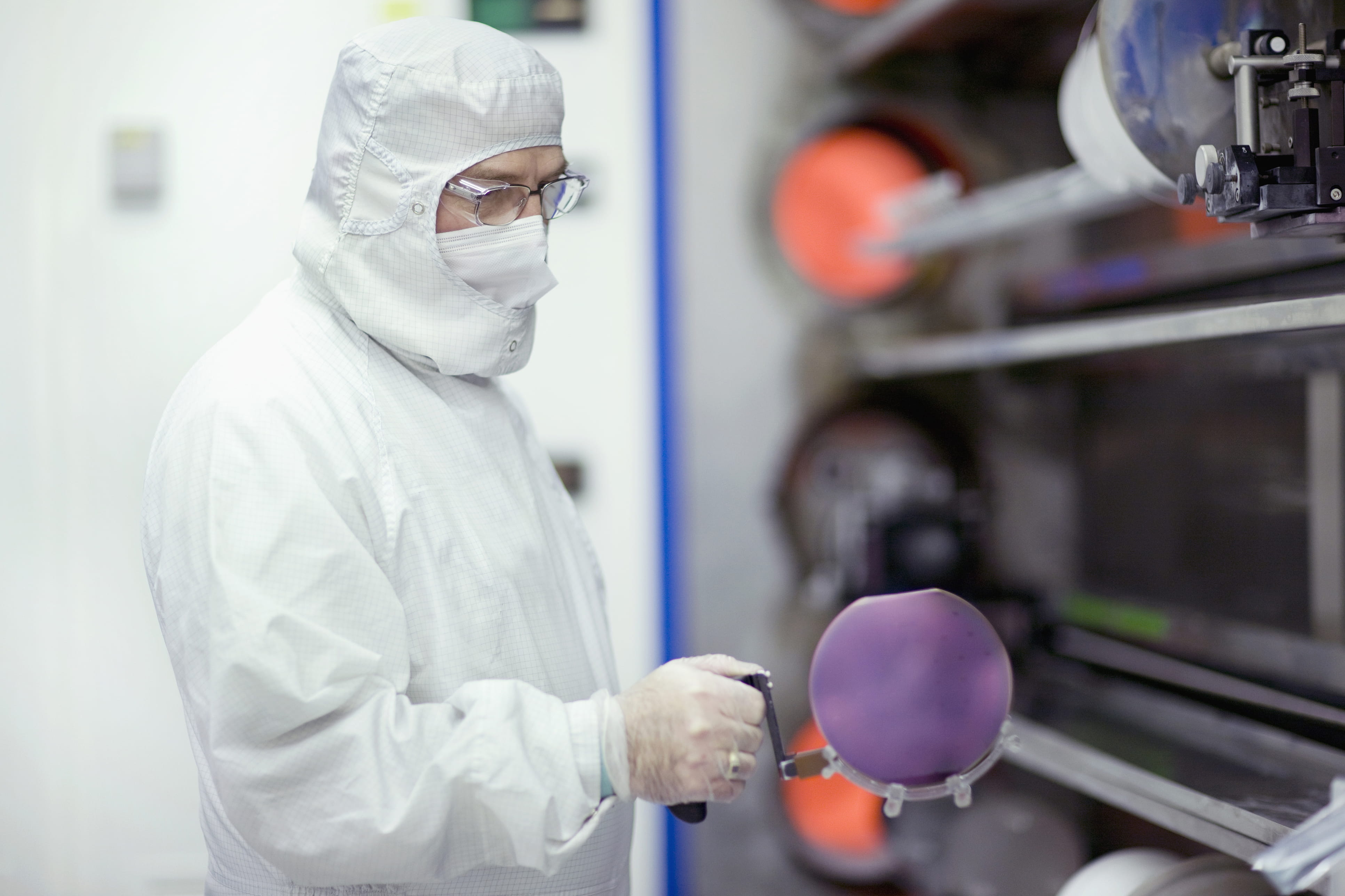 Engineer in clean suit holding silicon wafer in clean room